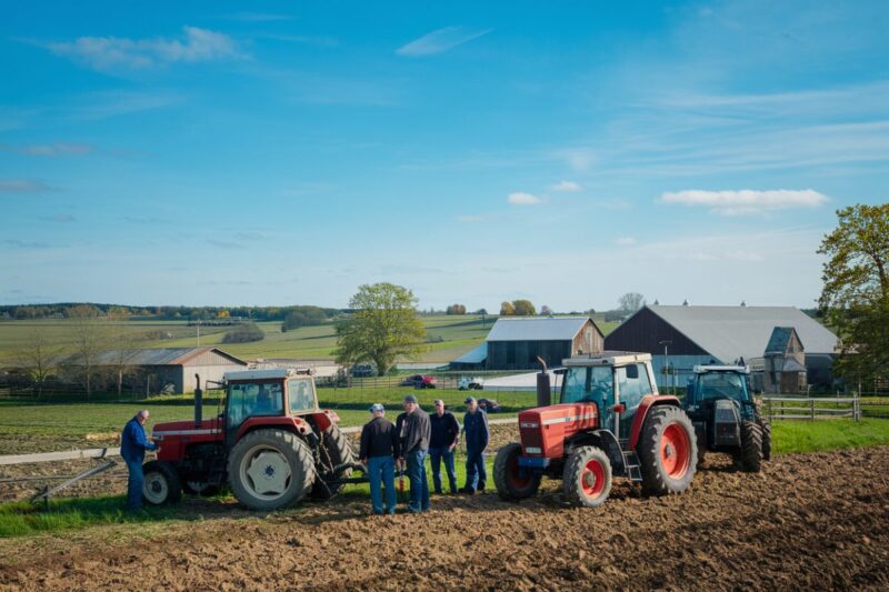 Paysage rural avec des agriculteurs discutant pr&egrave;s de leurs tracteurs.